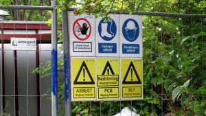 Skilte på hegnet rundt om skolen advarer mod PCB, bly og asbest. Foto: Rolf Larsen.